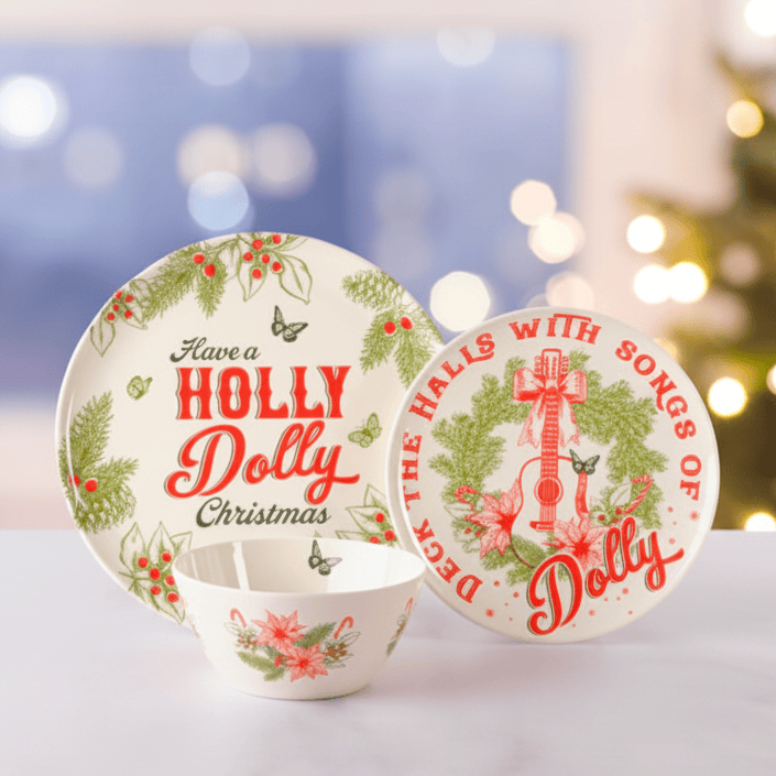 A Christmas-themed ceramic dinnerware set featuring a plate, a bowl, and a coaster. The white ceramic pieces are decorated with red and green holiday illustrations, including pine branches, red berries, a guitar, and festive text reading 'Have a HOLLY Dolly Christmas' and 'DECK THE HALLS WITH SONGS OF Dolly'.