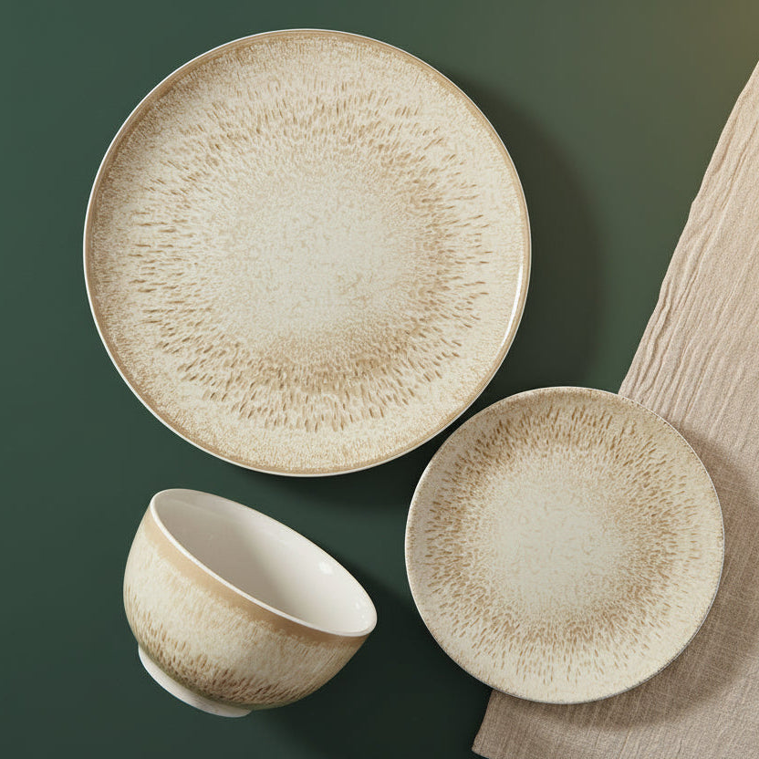 Three-piece ceramic dinnerware set with a textured, speckled beige and cream glaze, including a large plate, a bowl, and a smaller plate, arranged on a dark green background next to a matching beige textured cloth napkin.