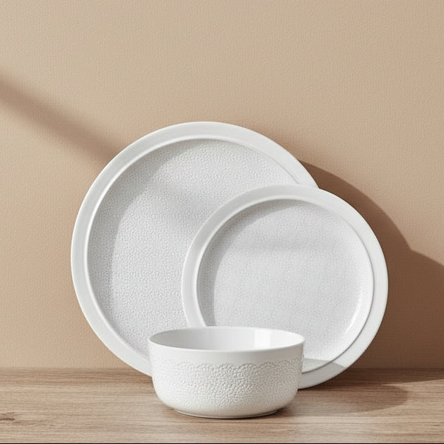 White ceramic dinnerware set on a wooden shelf against a white tiled wall.