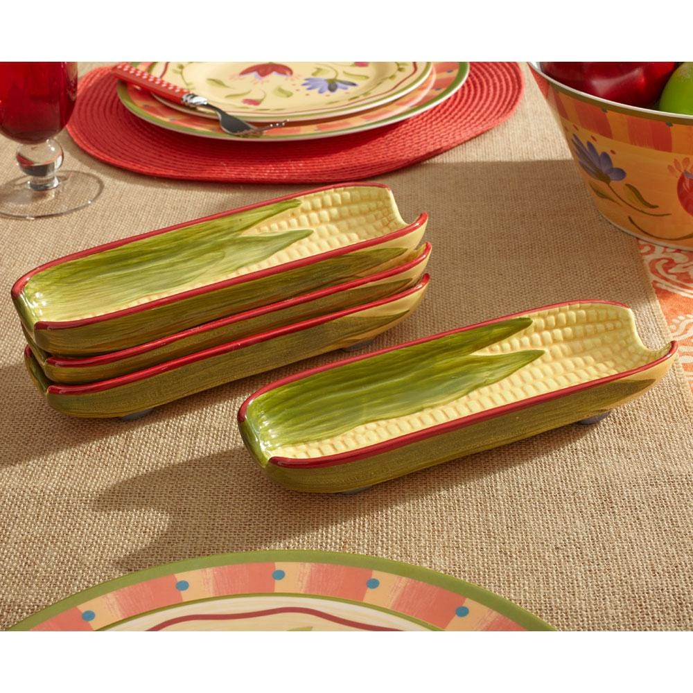 Napoli corn shaped dishes arranged on a table with place settings and a fruit bowl in the background.